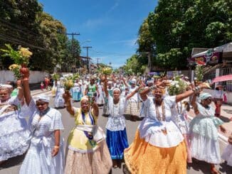 um grupo de mulheres culturalmente chamadas de baianas desfilam juntas acenando e sorrindo