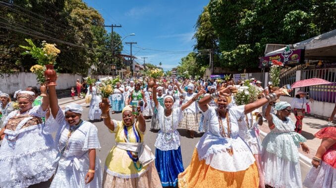 um grupo de mulheres culturalmente chamadas de baianas desfilam juntas acenando e sorrindo